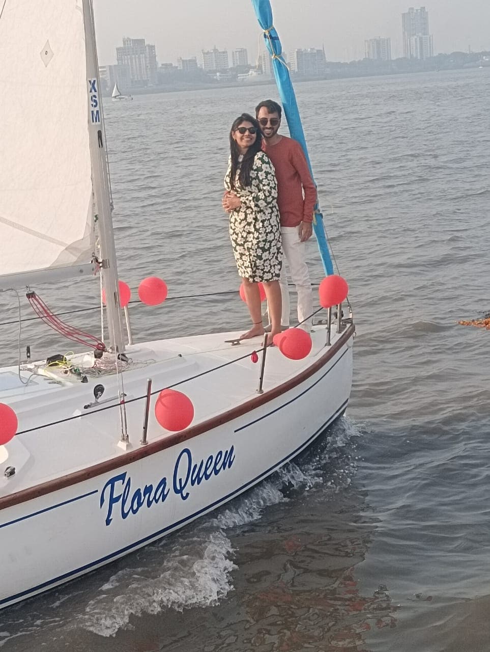 A couple standing at the bow of Flora Queen with the Mumbai skyline in the distance