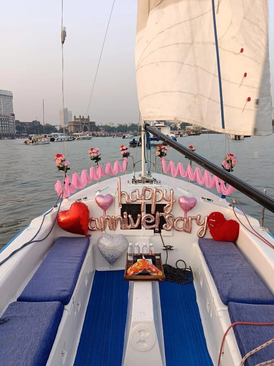 A happy anniversary balloon display on the bow with pink drapes and the Gateway of India behind