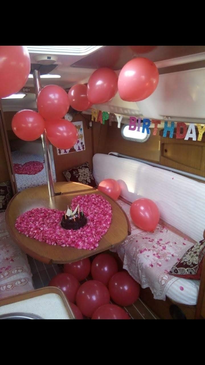 A birthday cake set on a heart of rose petals with balloons and a Happy Birthday banner