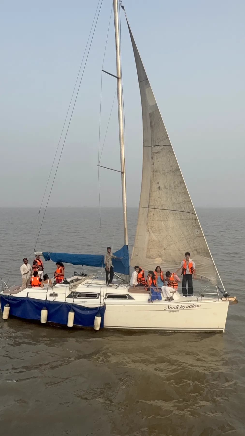 A group of guests in orange life jackets seated along the deck as Nauti by Nature sails