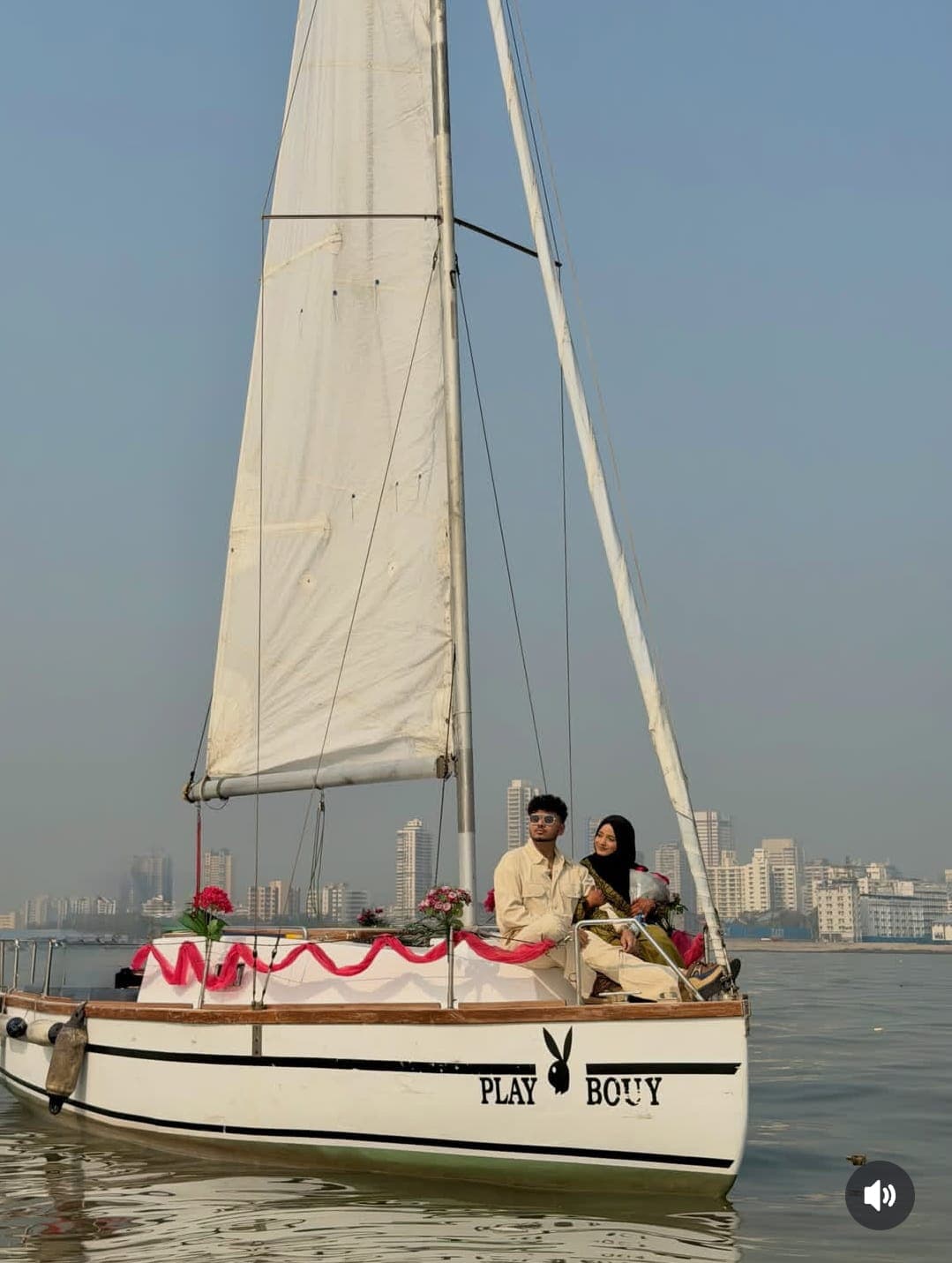 A couple seated on the bow with the Playboy nameplate and Mumbai skyline behind