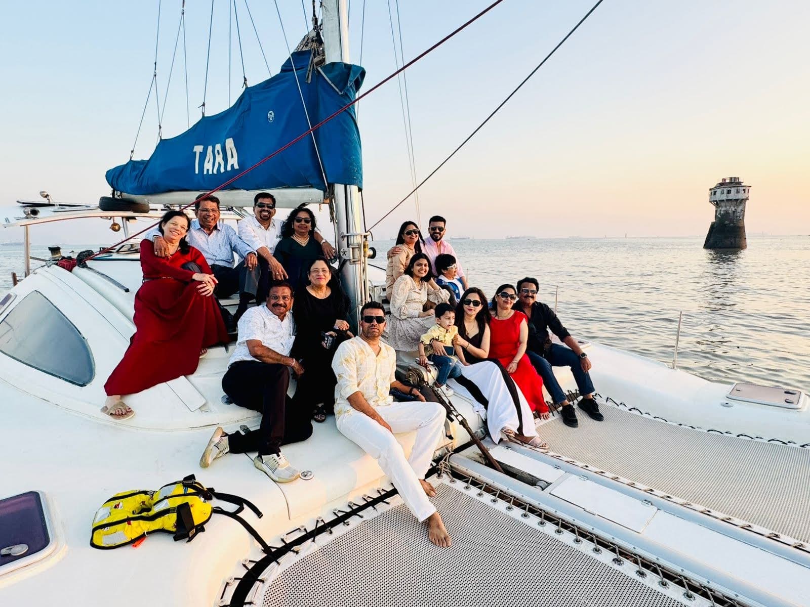 A large group photo on Tara's foredeck at sunset with the coastal battery fort behind
