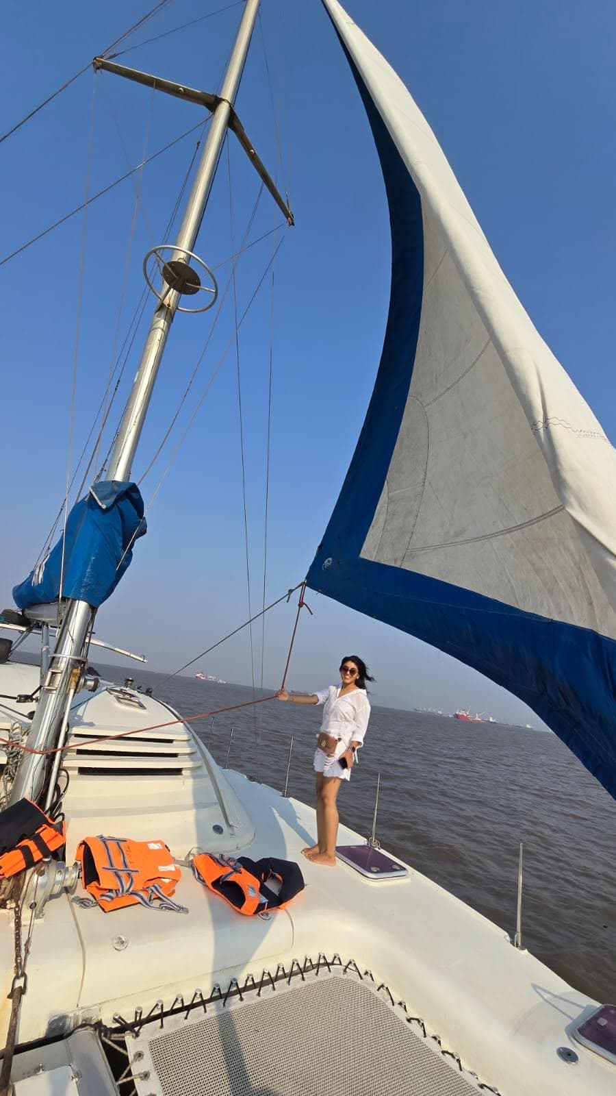 A guest standing at the bow holding the sail line under clear skies