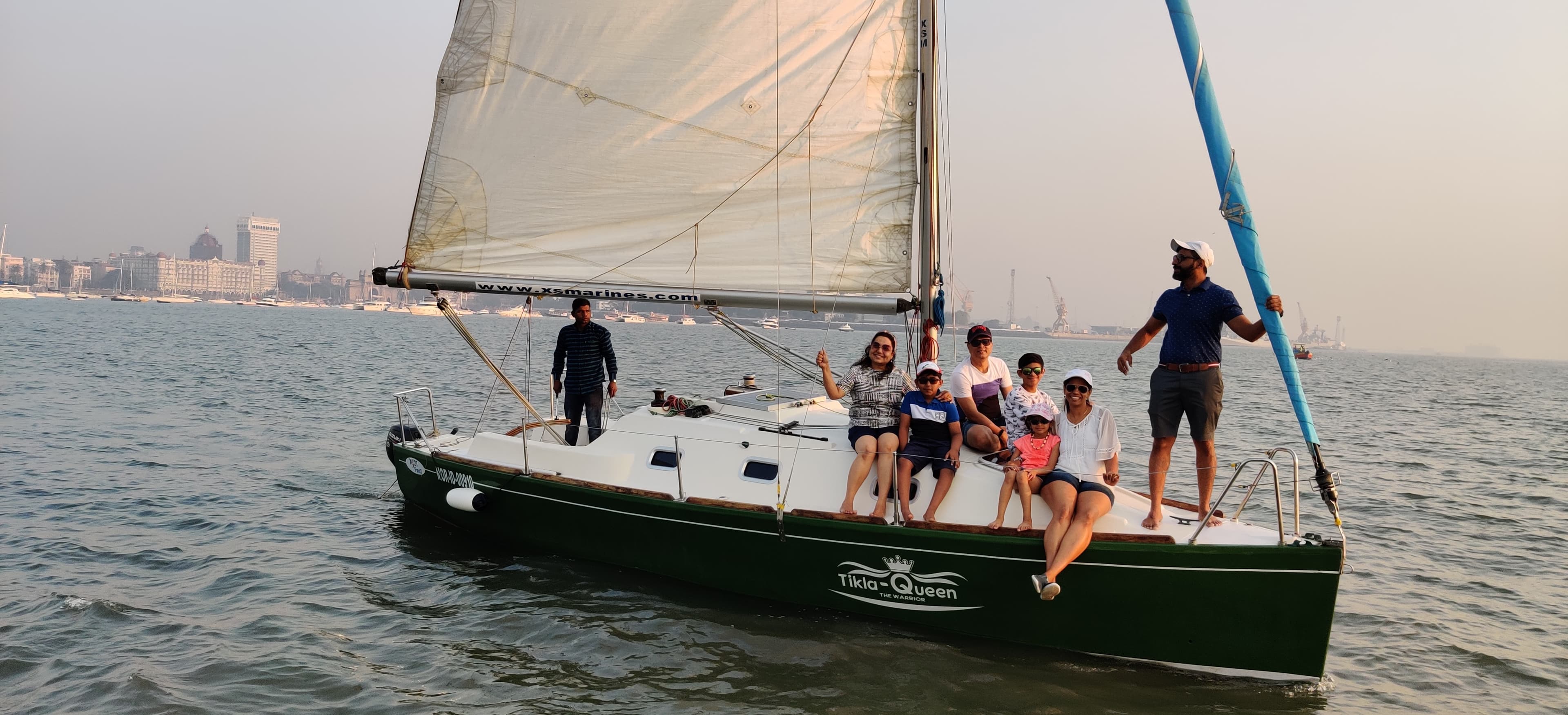 Tikla Queen under sail with a family aboard and the Mumbai skyline behind