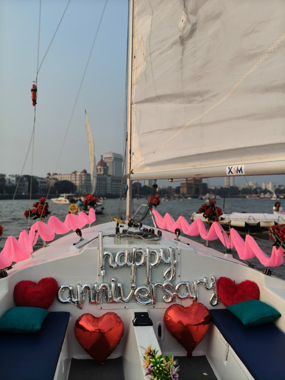 A 'Happy Anniversary' balloon display at the bow with the Gateway of India and Taj Mahal Palace visible behind