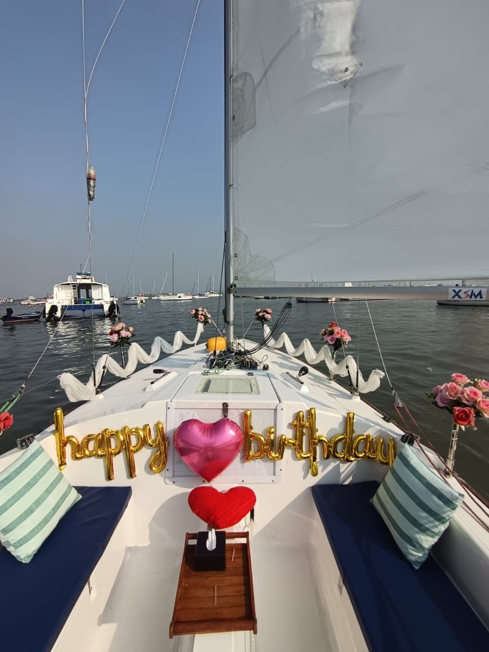 A 'Happy Birthday' balloon display at the bow with a pink heart balloon and fresh roses, harbour boats behind
