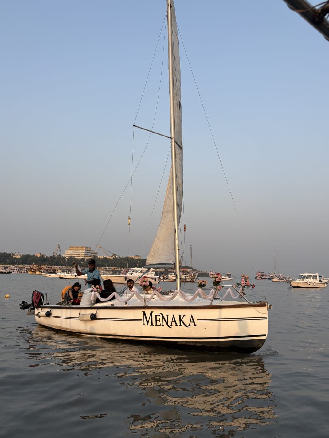 A guest in a red dress holding a bouquet of flowers at the bow under sail
