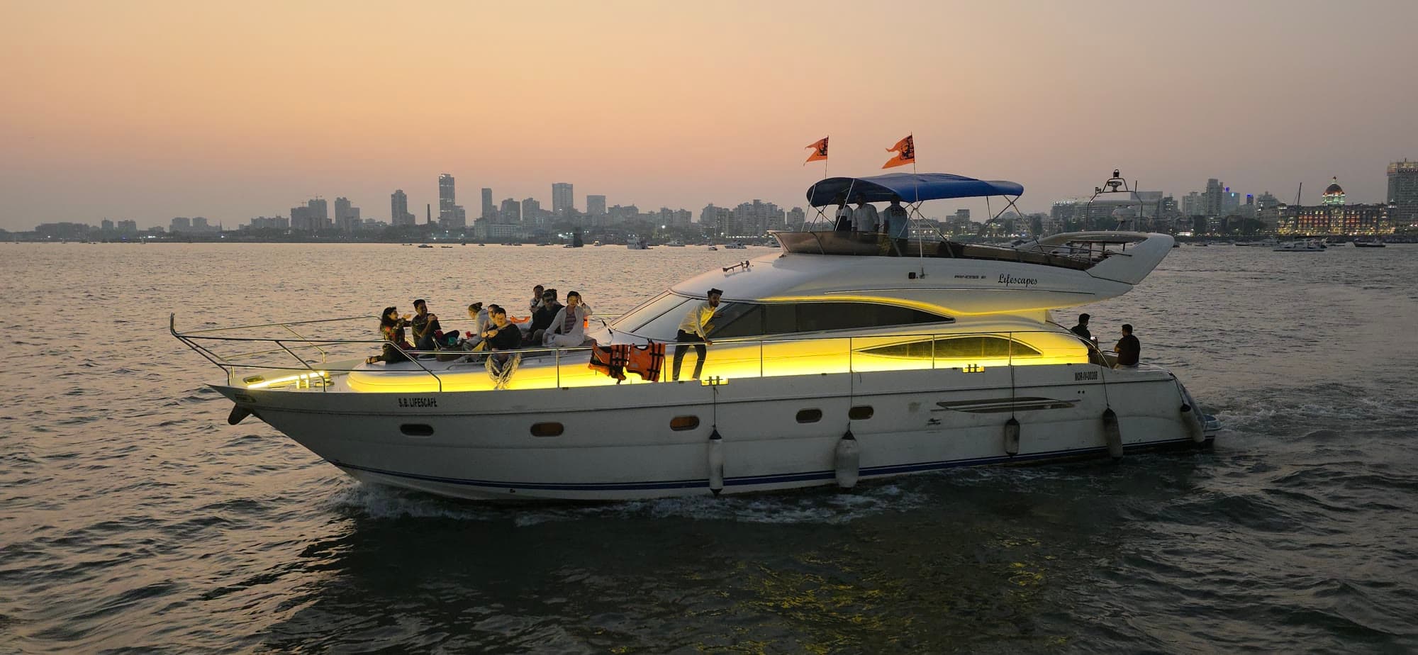 Princess 61 motor yacht Lifescapes cruising past the Mumbai skyline at dusk with guests on deck