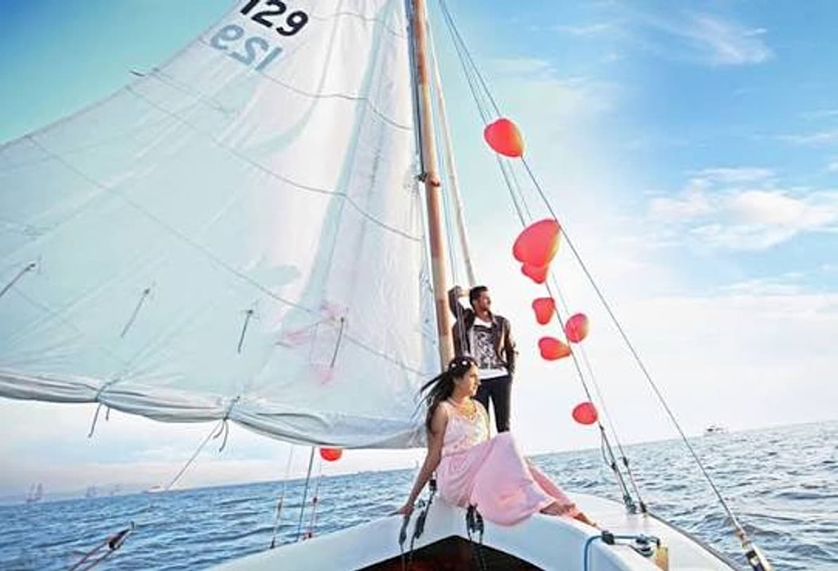 A couple on a sailboat bow with red heart balloons trailing from the rigging